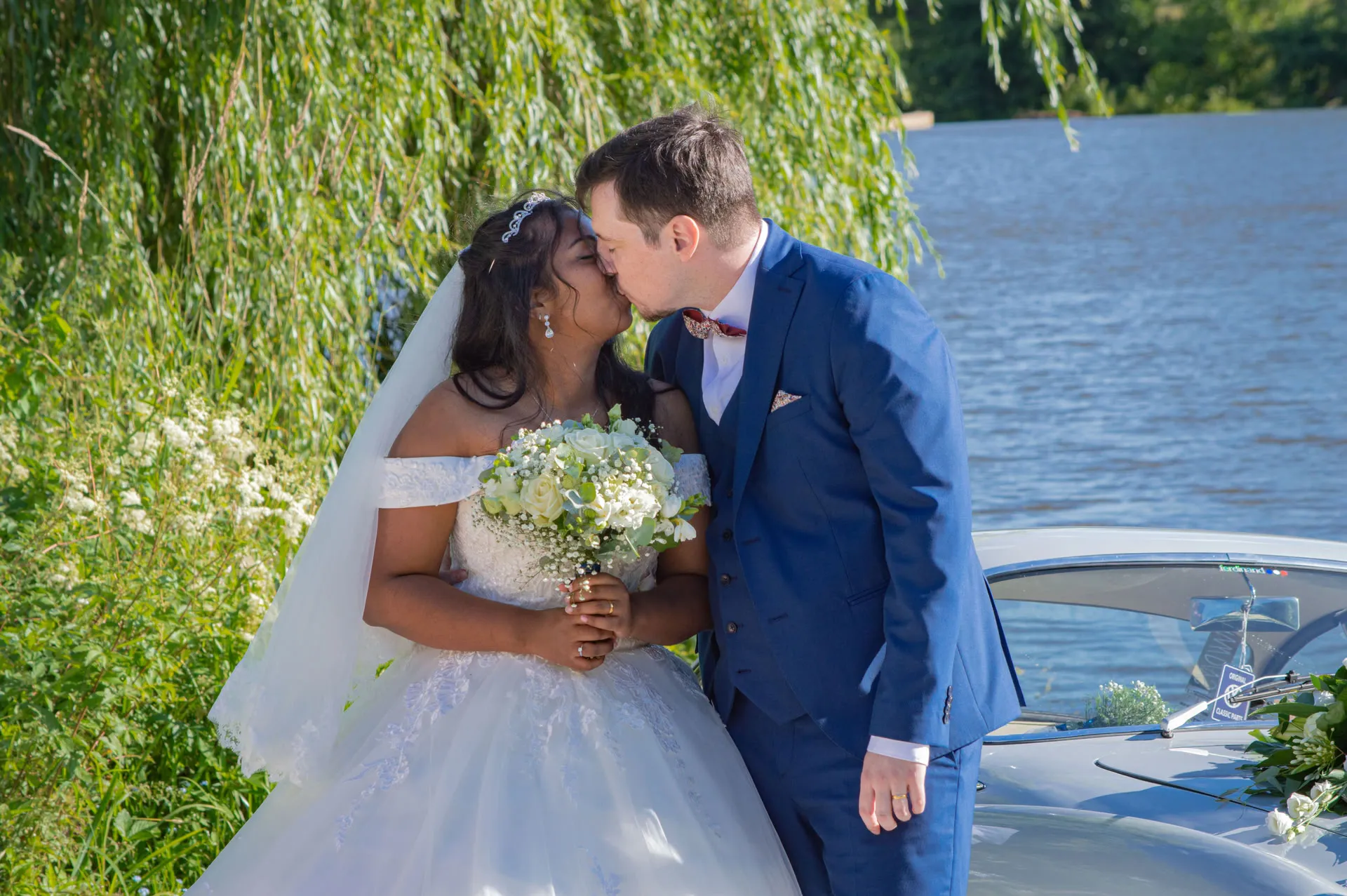 Mariage, couple qui pose et se regardent devant la voiture et un joli paysage